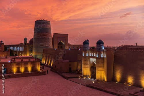 Historic architecture of Kalta Minor minaret and Kuhna Ark with illumination at sunset in Khiva, Uzbekistan. photo