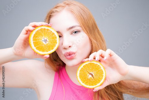 Young smiling woman holding juicy halves of orange in her hands near eyes isolated on gray background. Healthy eating concept. Diet.	