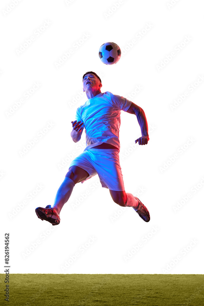 Naklejka premium Soccer player jumps leaping prepares to head soccer ball, with his body twisted in motion on field in neon light against white studio background. Concept of sport, competition, tournament, movement