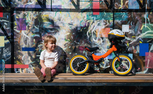 Active child. Sport for kids. Happy smiling child sitting after riding a balance bike against graffiti wall. Little girl and balance bike.