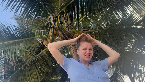 woman hiding her head under a coconut tree. carefully falling coconuts. hiding your head concept
