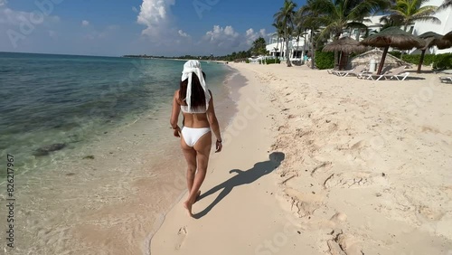 A sexy young woman enjoying a white sandy beach in the Riviera Maya, as she strolls along the pier over the crystal clear turquoise Caribbean water and heads to her resort in Mexico.