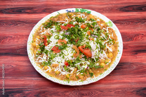 Spicy Chotpoti include chickpea, tomato, onion, cabbage, chilli, coriander, and sauce served in plate isolated on wooden table side view of bangladeshi street food