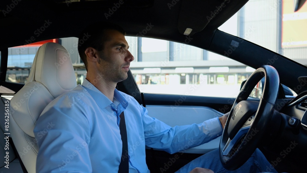 Profile of handsome businessman driving a modern electric car at urban road. Male successful entrepreneur riding on electrical vehicle at city. Young man commuting to work at sunny day. Slow motion Profile of handsome businessman driving a modern electric car at urban road. Male successful entrepreneur riding on electrical vehicle at city. Young man commuting to work at sunny day. Slow motion