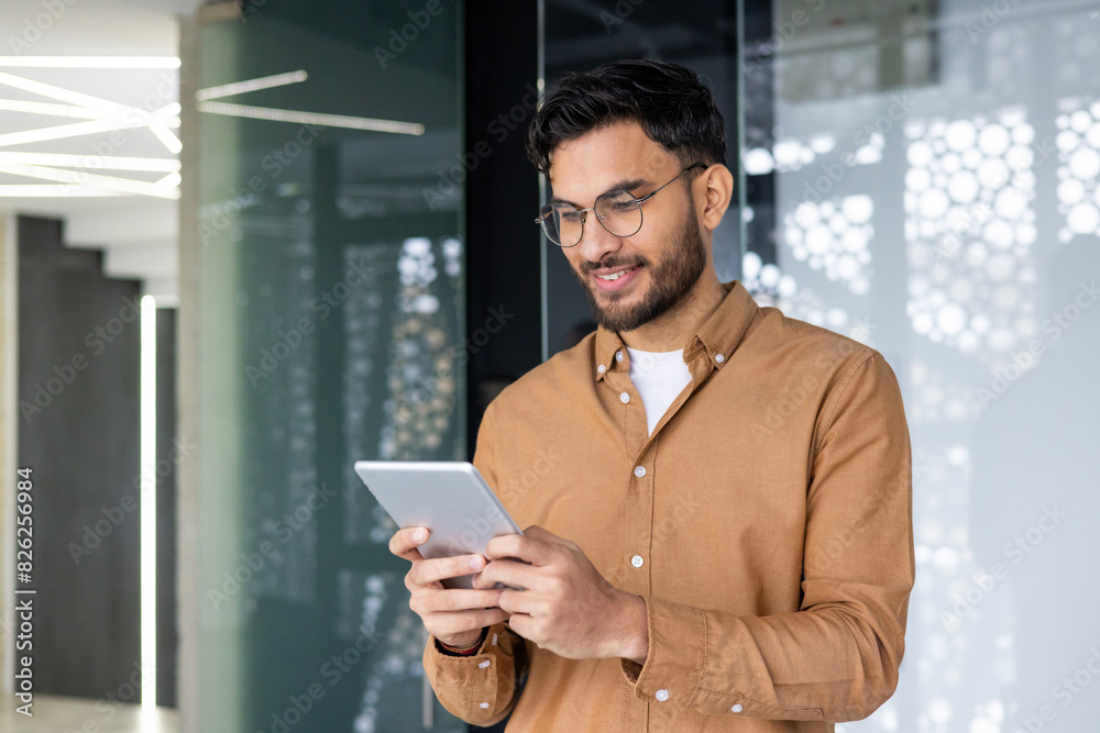 Young smiling Muslim male programmer and designer standing in modern office and using tablet Young smiling Muslim male programmer and designer standing in modern office and using tablet