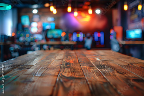 A wooden table in the foreground with a blurred background of a gaming cafÃ©. The background features rows of gaming PCs, comfortable gaming chairs, colorful LED lights, and posters of popular games.  © grey