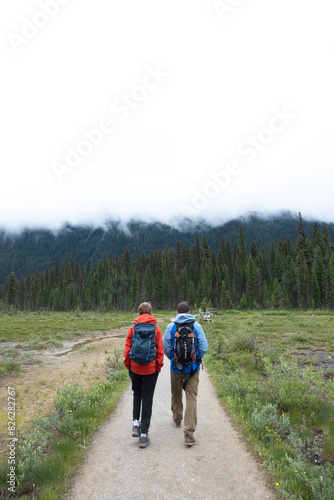 Two people walk away wearing backpacks on a dirt trail.