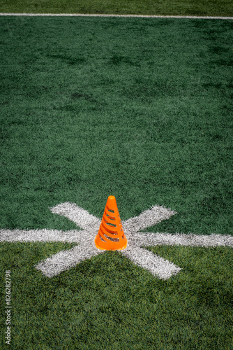 An orange athletic cone on a turf football field.