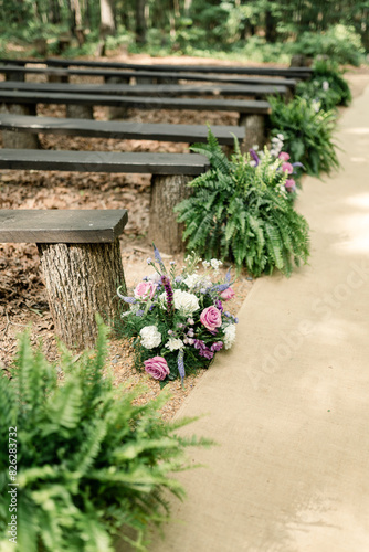 Floral arrangements and benches along an outdoor wedding aisle