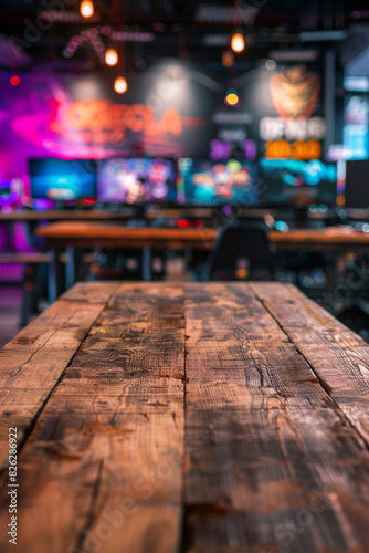 A wooden table in the foreground with a blurred background of a gaming cafÃ©. The background features rows of gaming PCs, comfortable gaming chairs, colorful LED lights, and posters of popular games.  © grey
