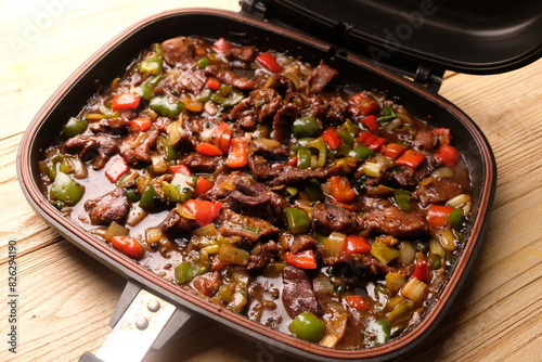 closeup of black pepper beef in double fry pan. cooked with black pepper, red and green peppers, onions, oyster sauce, pepper and spices.