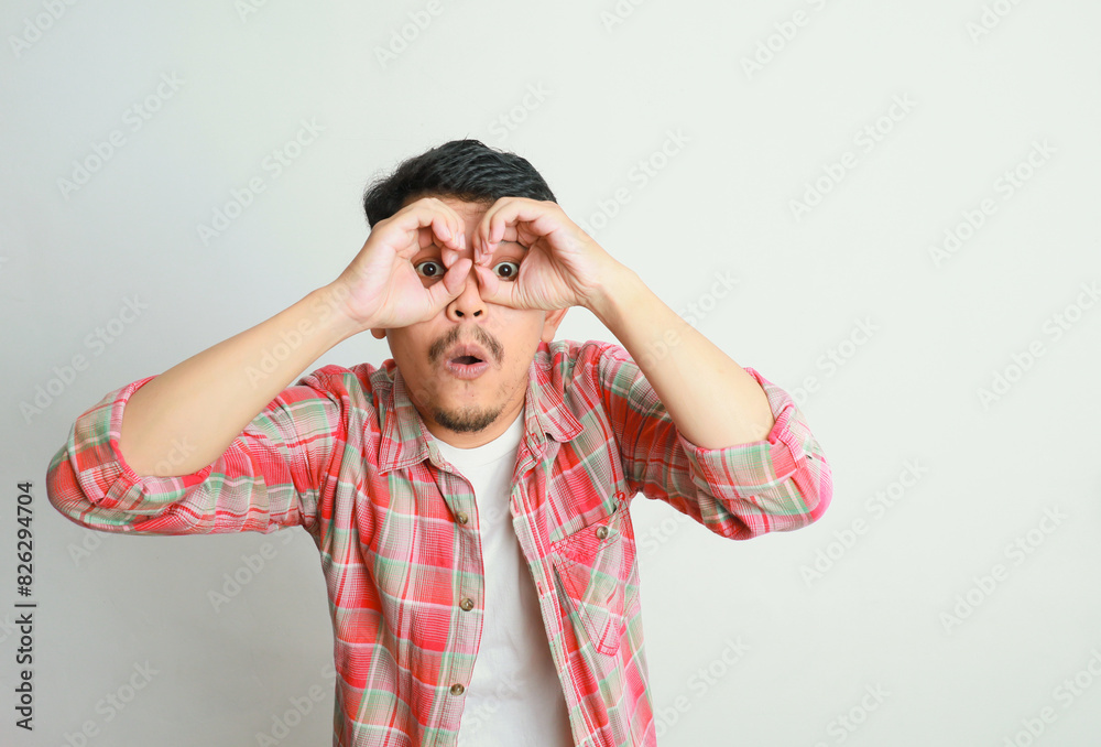 portrait of excited Asian man shocked gesture with both hands pretending to wear glasses