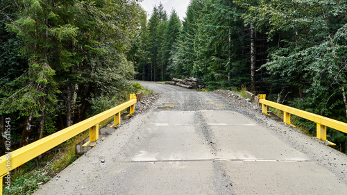 A remotesingle lane logging road bridge with yellow railings used by industrial logging trucks. photo