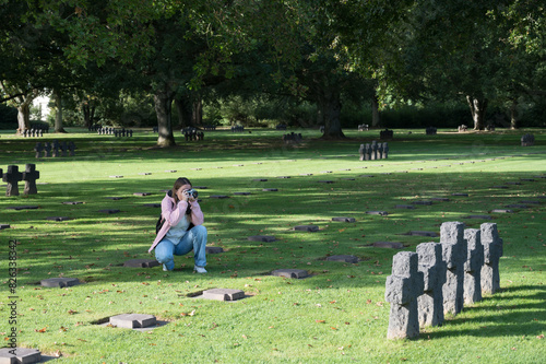 A young blonde woman crouched down taking photographs of the German cemetery of La Cambe photo