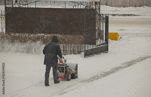 Robotnik clears snow from the sidewalk with a manual snowplow driven by a gasoline engine. Fighting the after-effects of a snowstorm. The power of the winter element