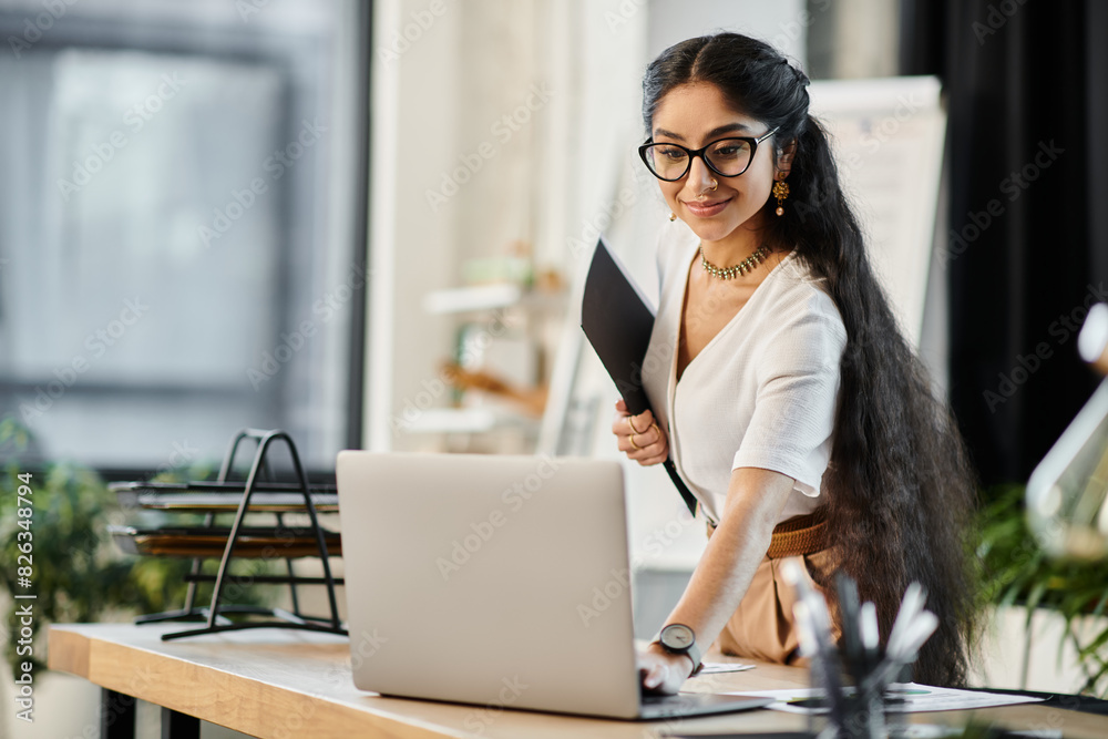 Fototapeta premium A stylish indian woman in glasses works diligently on a laptop in an office setting.