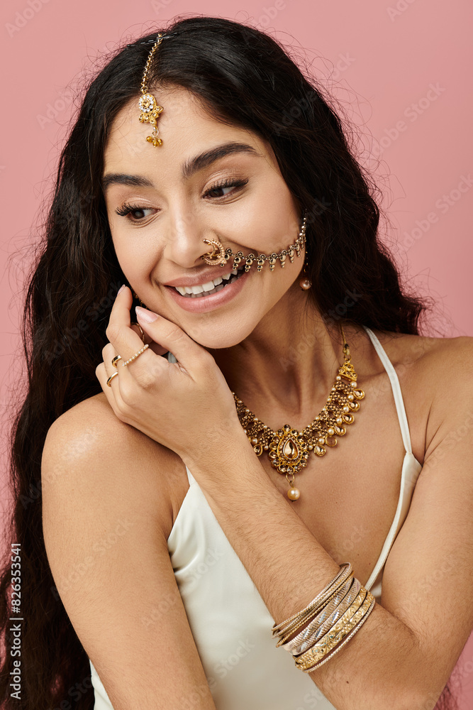 Young indian woman with long hair and gold jewelry poses gracefully against a vibrant pink backdrop. Young indian woman with long hair and gold jewelry poses gracefully against a vibrant pink backdrop.