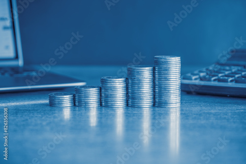 Up stack of money coins with laptop computer and calculator on a table representing money, finance, and investment. Business and financial concept with blue color filter. 