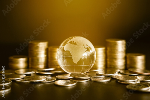 Small glass globe on golden money coin and stack of golden money coin in the background. Worldwide business and financial concept. 