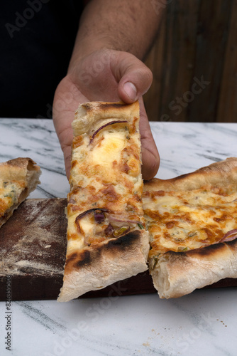 Gastronomy. Closeup view of a male caucasian hand holding a slice of mozzarella, provolone and blue cheese pizza with onions.