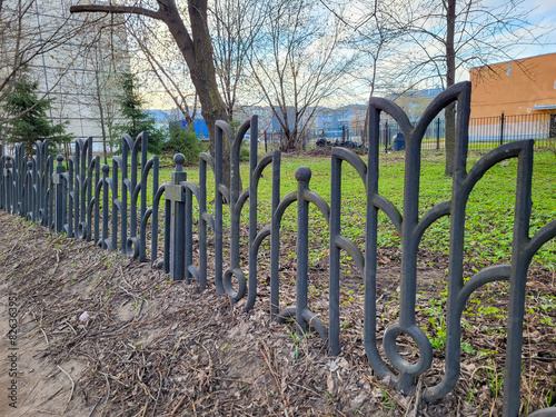 A low beautiful decorative wrought iron fence with artistic forging. Metal fence in close-up.