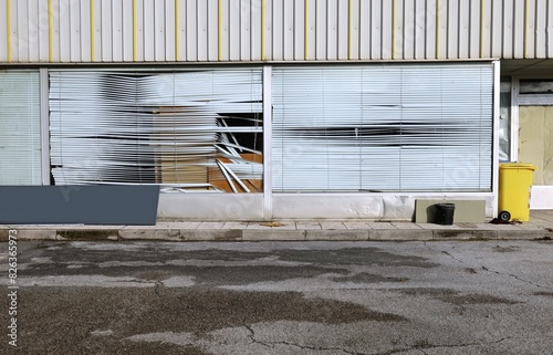 Abandoned store with large windows and damaged venetian blinds, at the roadside. Sidewalk and street in front. Grunge background for copy space.