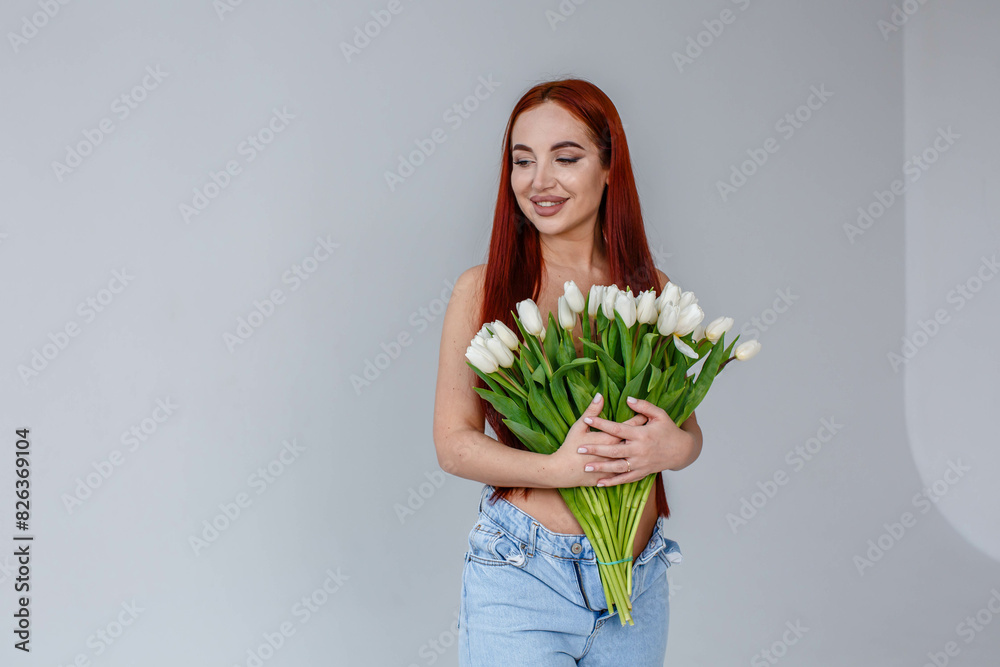Red-haired girl in jeans with white tulips posing on a white background