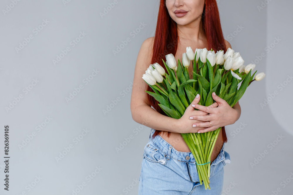 Red-haired girl in jeans with white tulips posing on a white background
