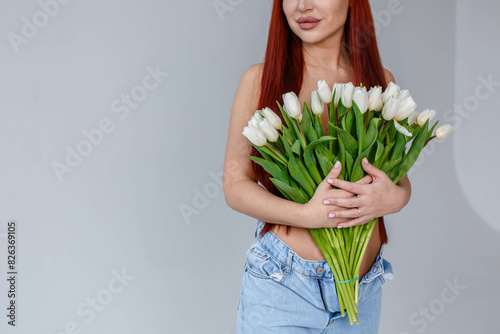 Obraz na płótnie Red-haired girl in jeans with white tulips posing on a white background
w salonie