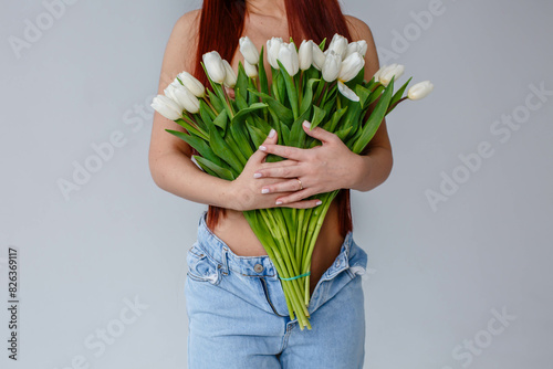 Obraz na płótnie Red-haired girl in jeans with white tulips posing on a white background
w salonie