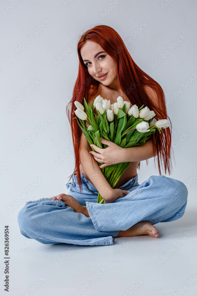 Red-haired girl in jeans with white tulips posing on a white background