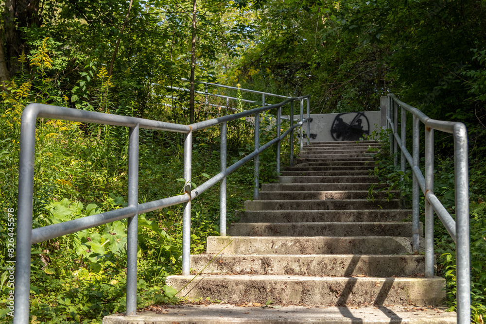 Concrete staircase with metal railings - leads up to forested area - shadows on steps - graffiti on wall at top. Taken in Toronto, Canada. Concrete staircase with metal railings - leads up to forested area - shadows on steps - graffiti on wall at top. Taken in Toronto, Canada.