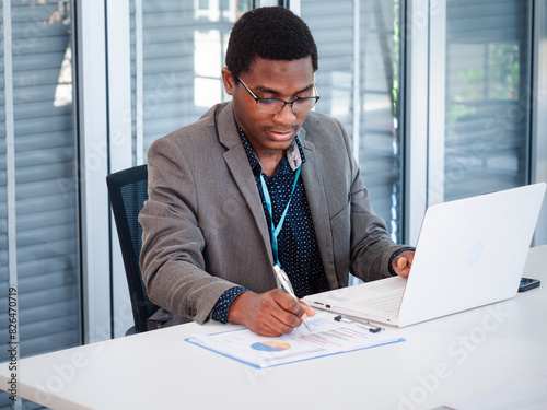 Portrait of African American project manager analyst documents looking at laptop computer screen doing online analyzing business data research thinking working sit at office desk.