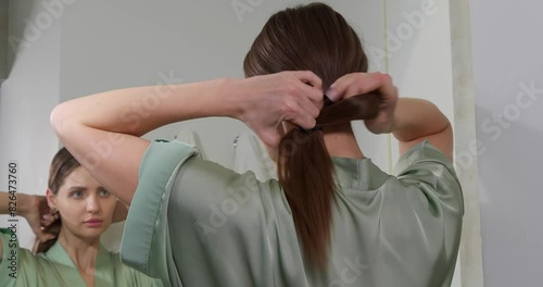 Beautiful woman tying hair up in ponytail near mirror at home