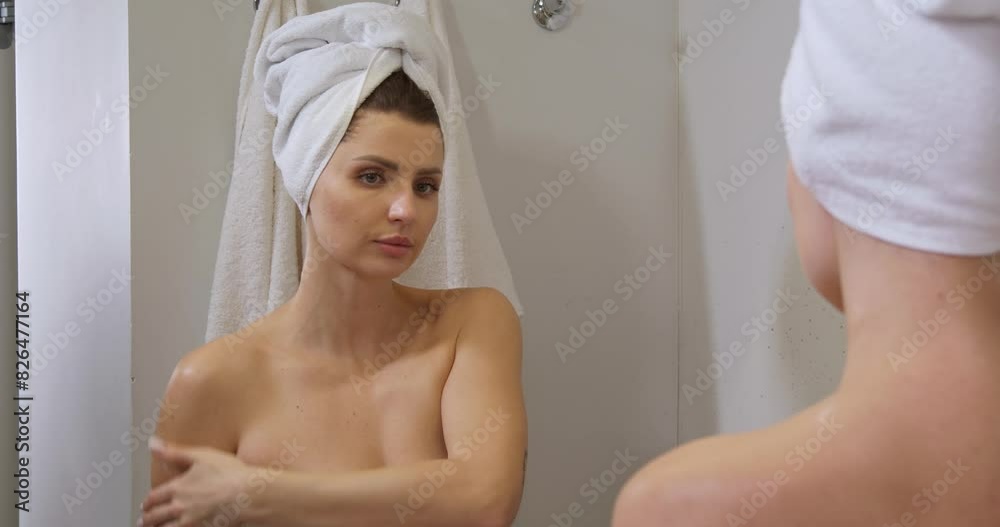 Beautiful woman with wet hair wrapped in towel applying body cream near mirror in bathroom Beautiful woman with wet hair wrapped in towel applying body cream near mirror in bathroom