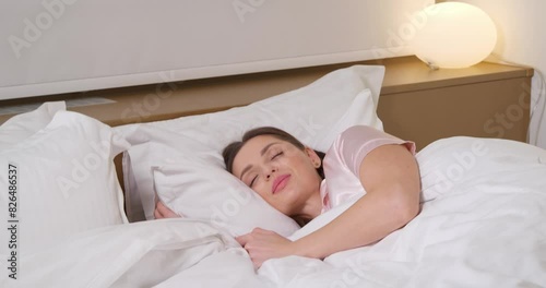 Beautiful woman going to sleep in bed. Camera moving towards her