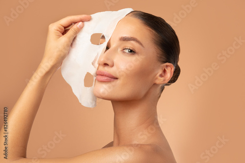 Bilde på lerret Beautiful European lady removing moisturizing white fabric sheet mask from her f