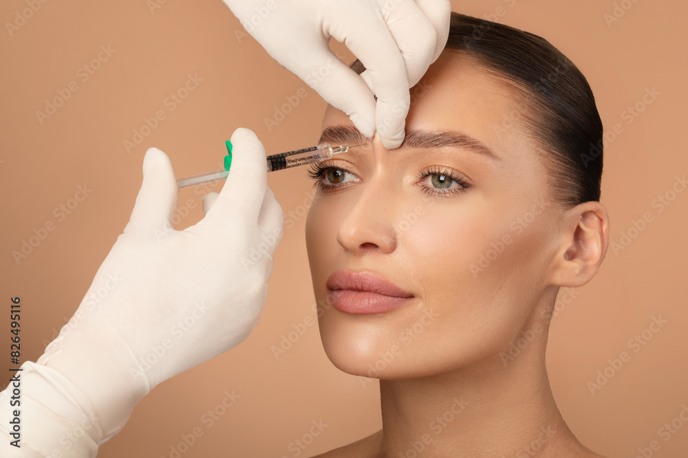 Obraz premium Beautician making hyaluronic acid injection for glabella facial rejuvenation procedure, young European woman getting cosmetic injection between eyebrows
