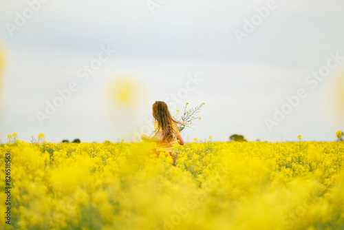 Long haired girl playing in vibrant canola field in full bloom during Spring season photo