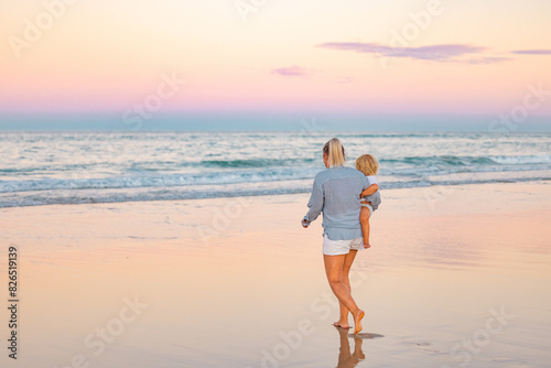 Single mother carrying son on the beach in twilight light. Sunset on the Gold Coast photo