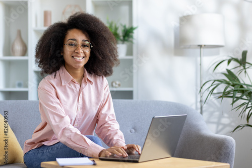 A woman happily works on her laptop in a home office with natural light and plants, creating a cozy and productive workspace. She looks professional and content in this modern setting