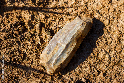 An ancient flint tool covered with a whitish patina lying on the ground, a Stone Age artifact at the discovery site photo