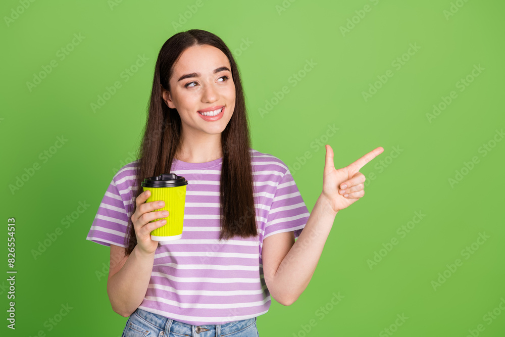 Photo of lovely young lady look point empty space hold paper cup dressed stylish striped violet garment isolated on green color background Photo of lovely young lady look point empty space hold paper cup dressed stylish striped violet garment isolated on green color background