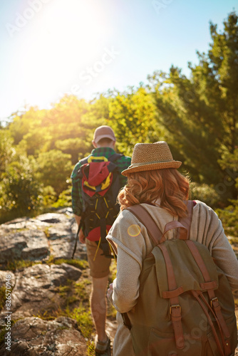 Nature, hiking and couple with sunshine, walking and adventure holiday in mountain from back. Trekking, man and woman on travel vacation together in park with trees, bush and outdoor climbing date
