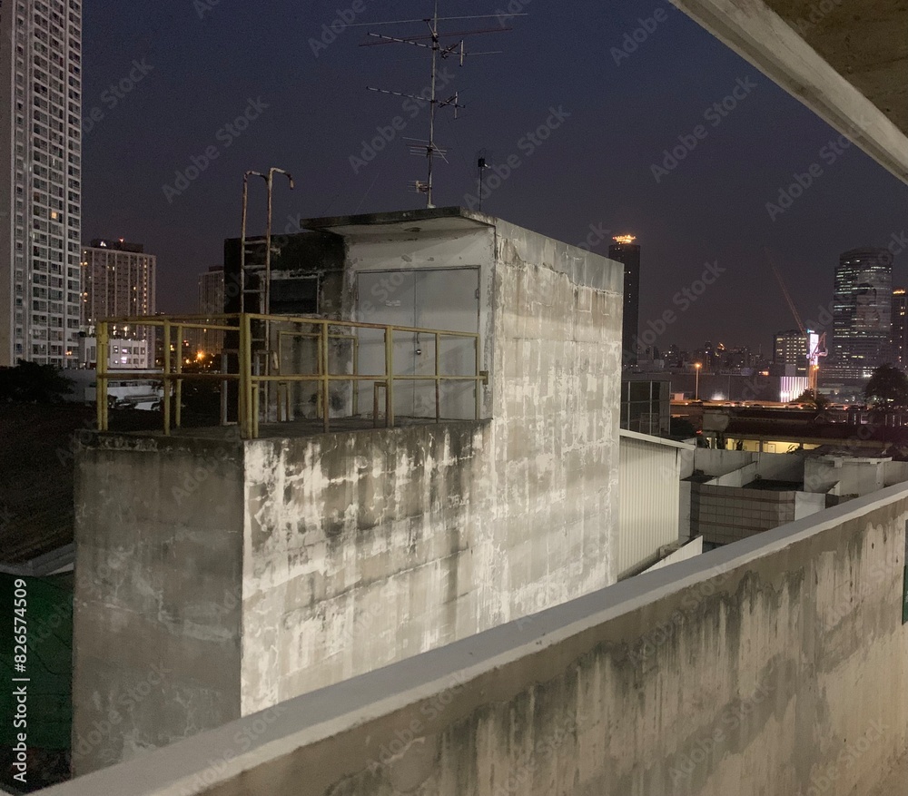 Obraz premium Night blur photo of rooftop on old building in Bangkok, Thailand with high sky building as background, deck with exit door and fence