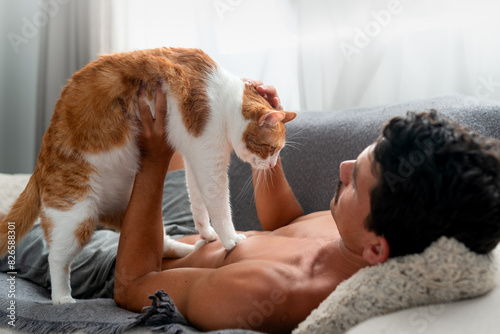 young man interacts with a brown and white cat on a sofa