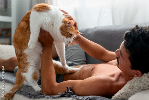 young man interacts with a brown and white cat on a sofa