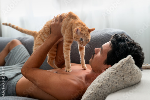 Brown tabby cat  on the chest of a young man lying on a sofa. The man strokes the cat's head . close up