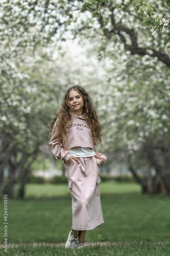 A beautiful toddler girl in a pink dress stands by a blooming white apple tree in the park and enjoys the beauty of a blooming garden, spring. A beautiful toddler girl in a pink dress stands by a blooming white apple tree in the park and enjoys the beauty of a blooming garden, spring.