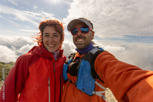 A man and a woman are smiling for a picture. The man is wearing a blue and orange jacket and the woman is wearing a red jacket